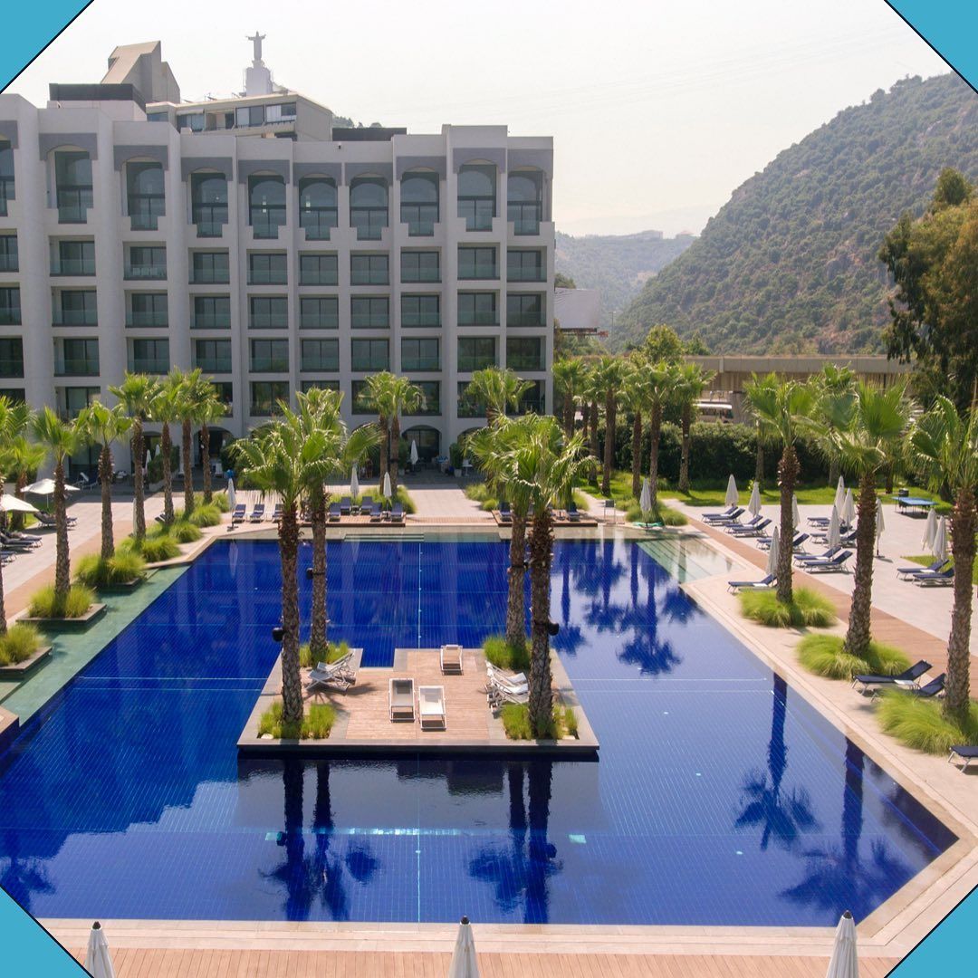 A large swimming pool surrounded by palm trees in front of a hotel