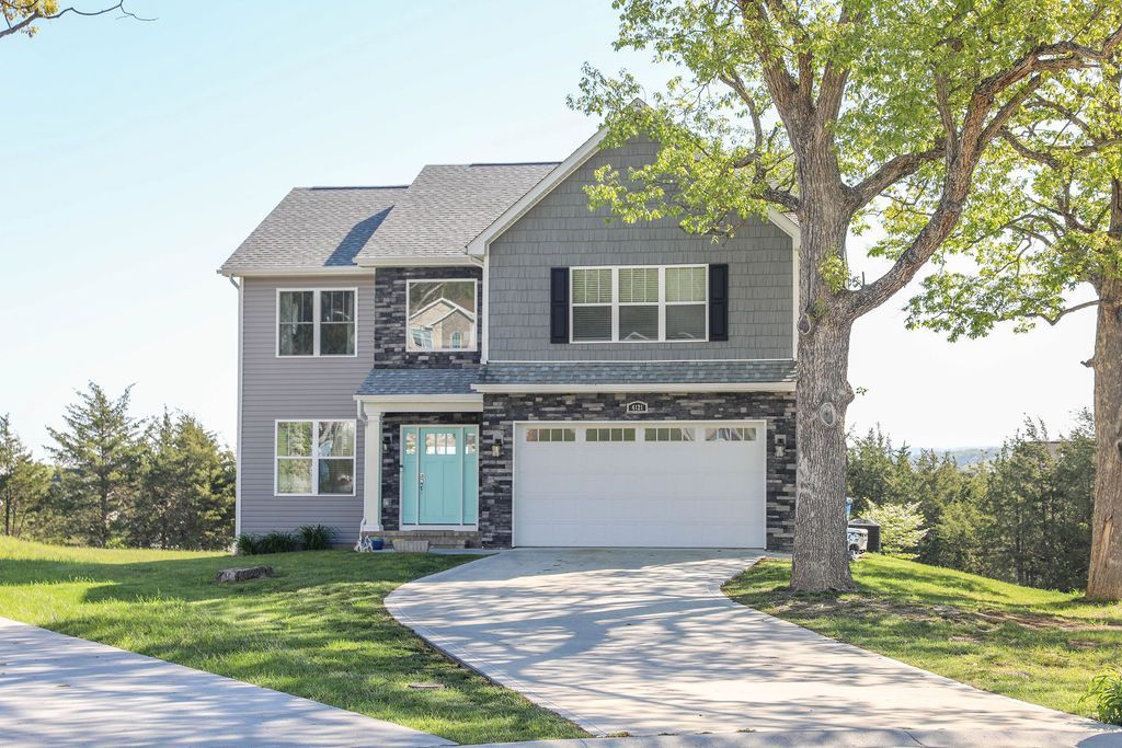 A large house with a blue door and a white garage door is sitting on top of a lush green hill.