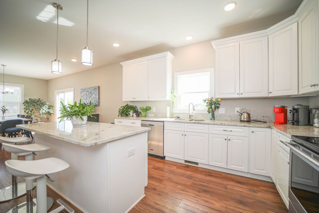 A kitchen with white cabinets , granite counter tops , stainless steel appliances and hardwood floors.