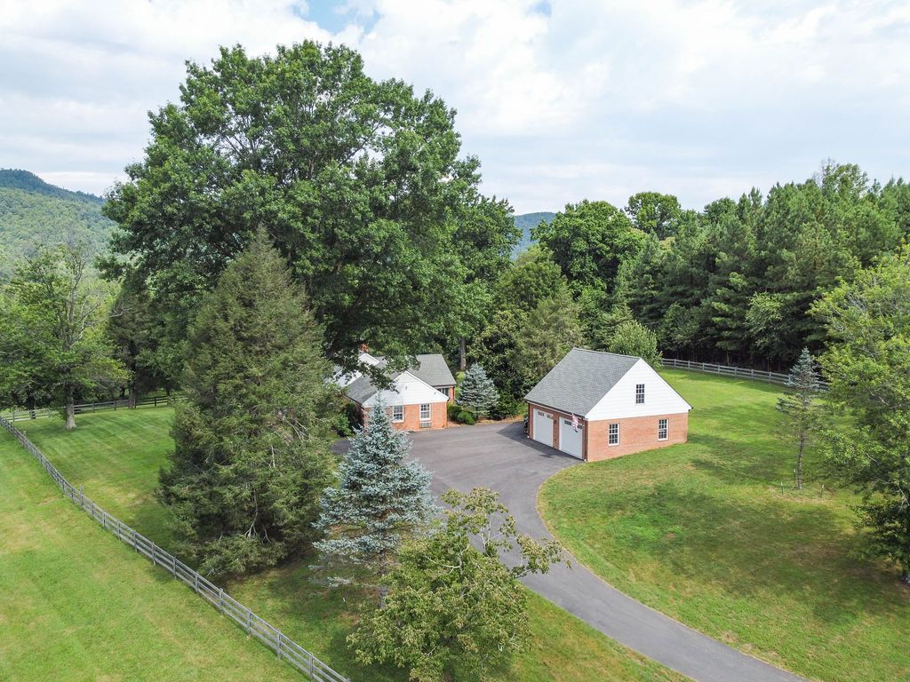 An aerial view of a house in the middle of a lush green field surrounded by trees.