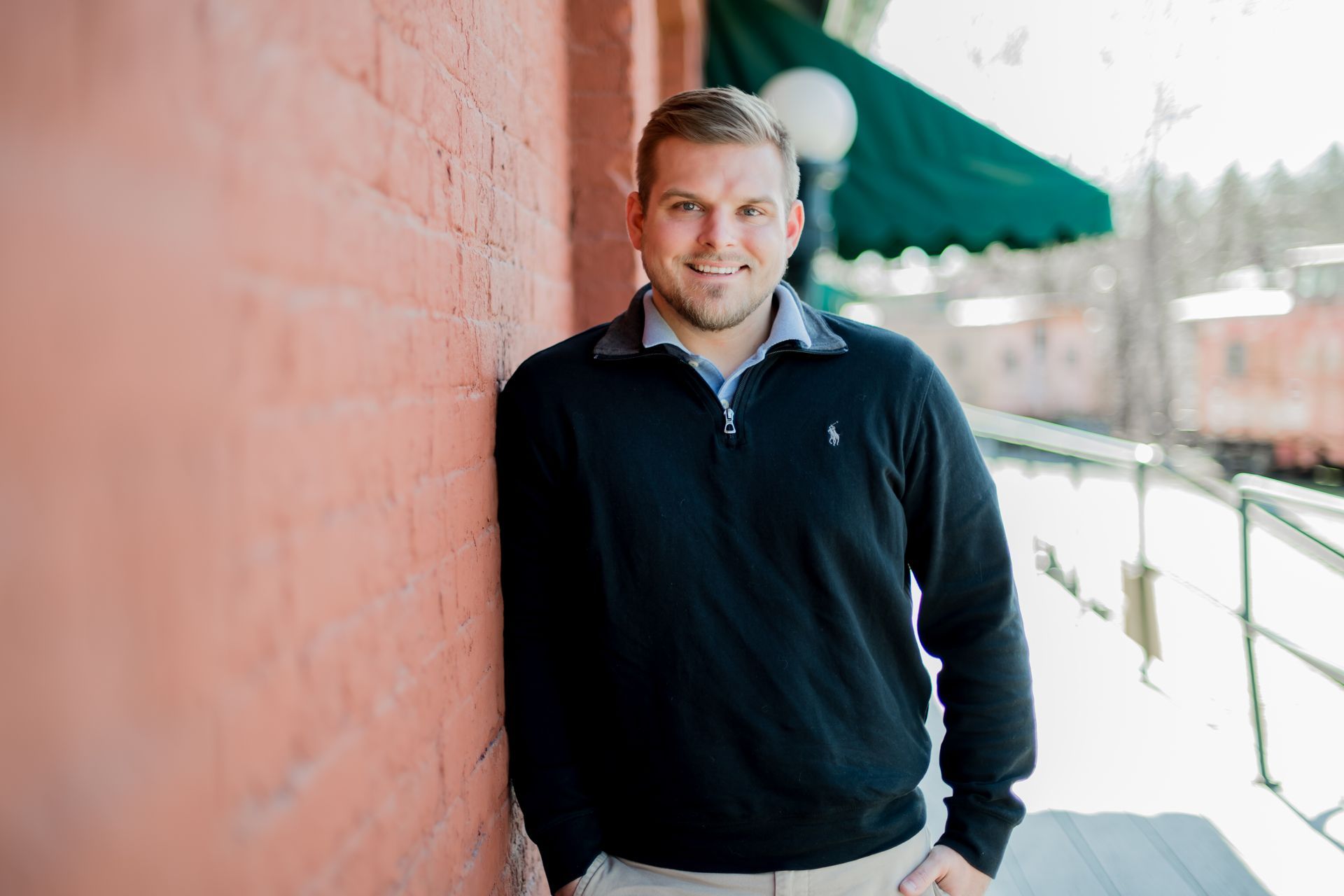 A man in a black sweater is leaning against a pink wall.