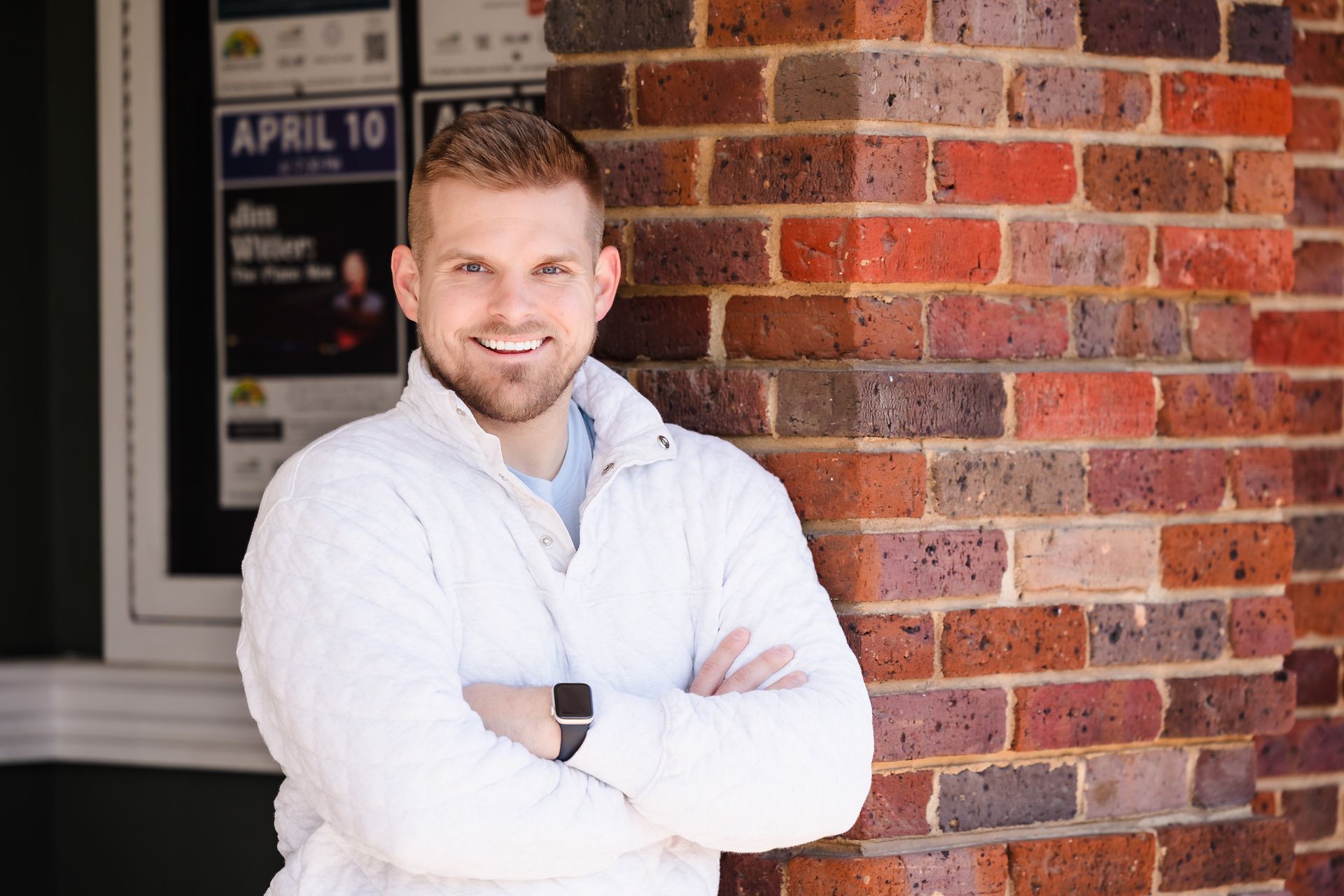 A man is standing in front of a brick wall with his arms crossed.