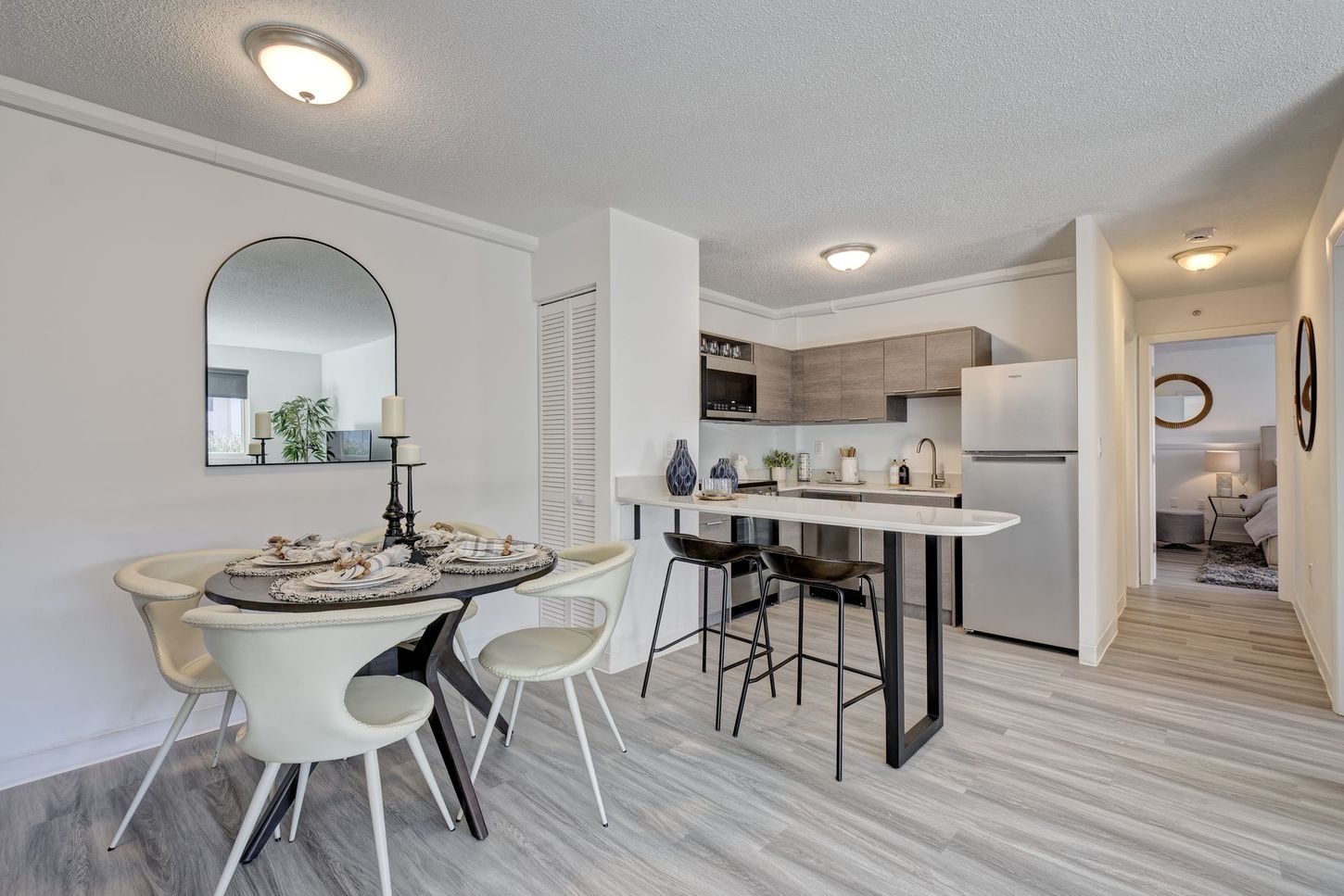 An open-concept dining area with kitchen: table set for four, breakfast bar, and stainless steel appliances.