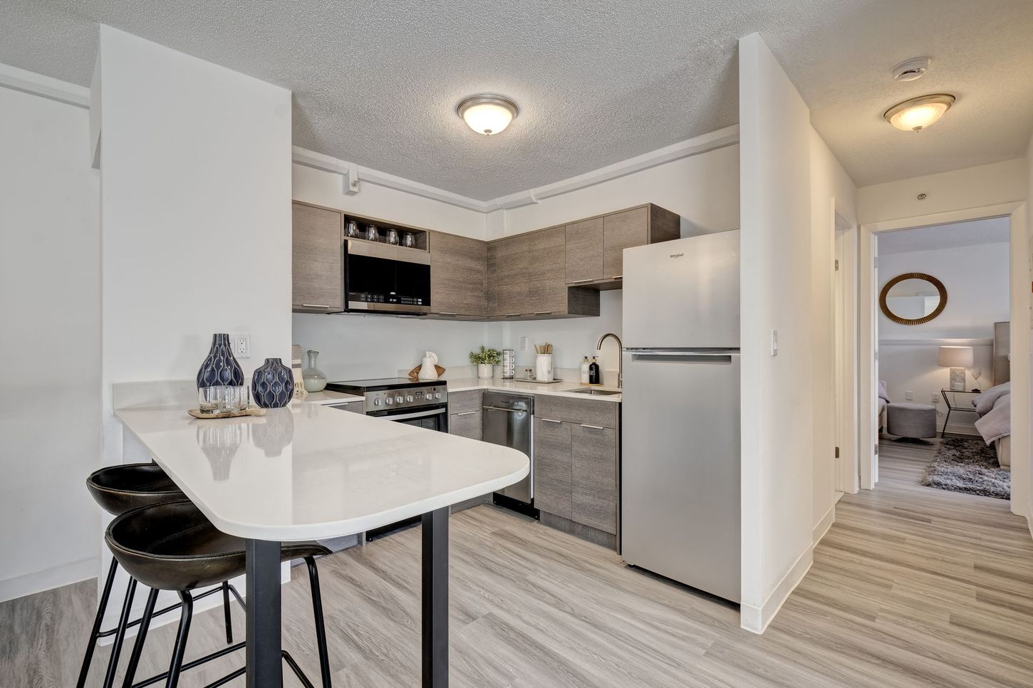 Small apartment kitchen with breakfast bar, stainless steel appliances, and hallway leading to bedroom.