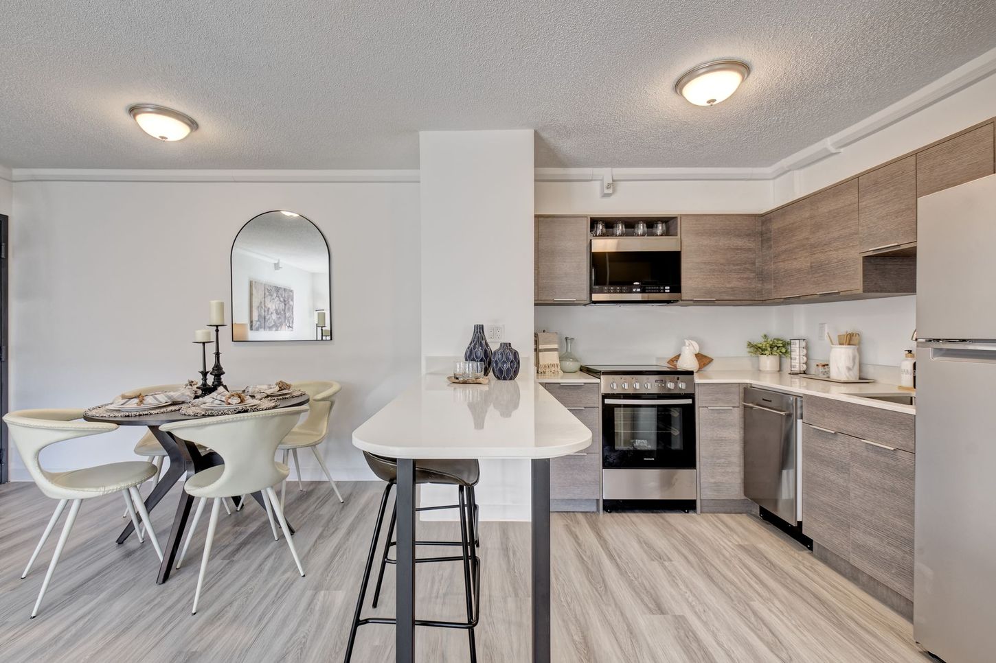 Modern kitchen and dining area with light wood cabinets, white countertops, and bar seating.