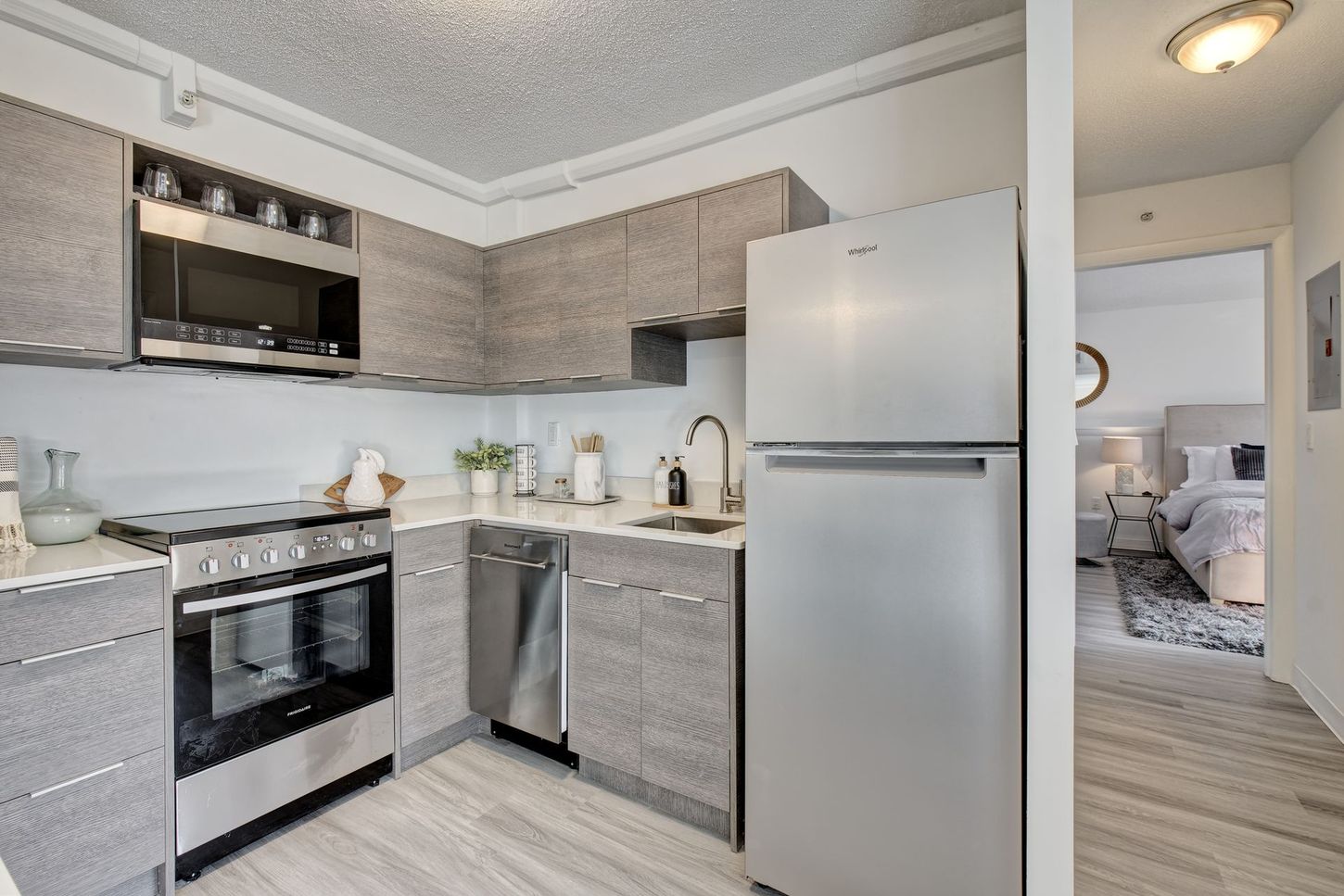 Modern kitchen with gray cabinets, stainless steel appliances, and a glimpse of a bedroom.