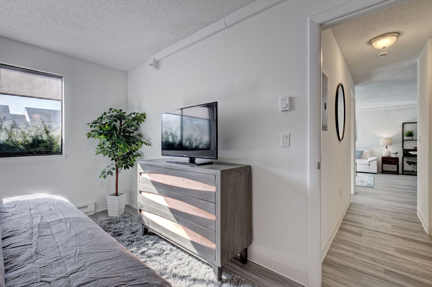Bedroom with TV on a dresser, a window with a shade, and a hallway leading to another room.