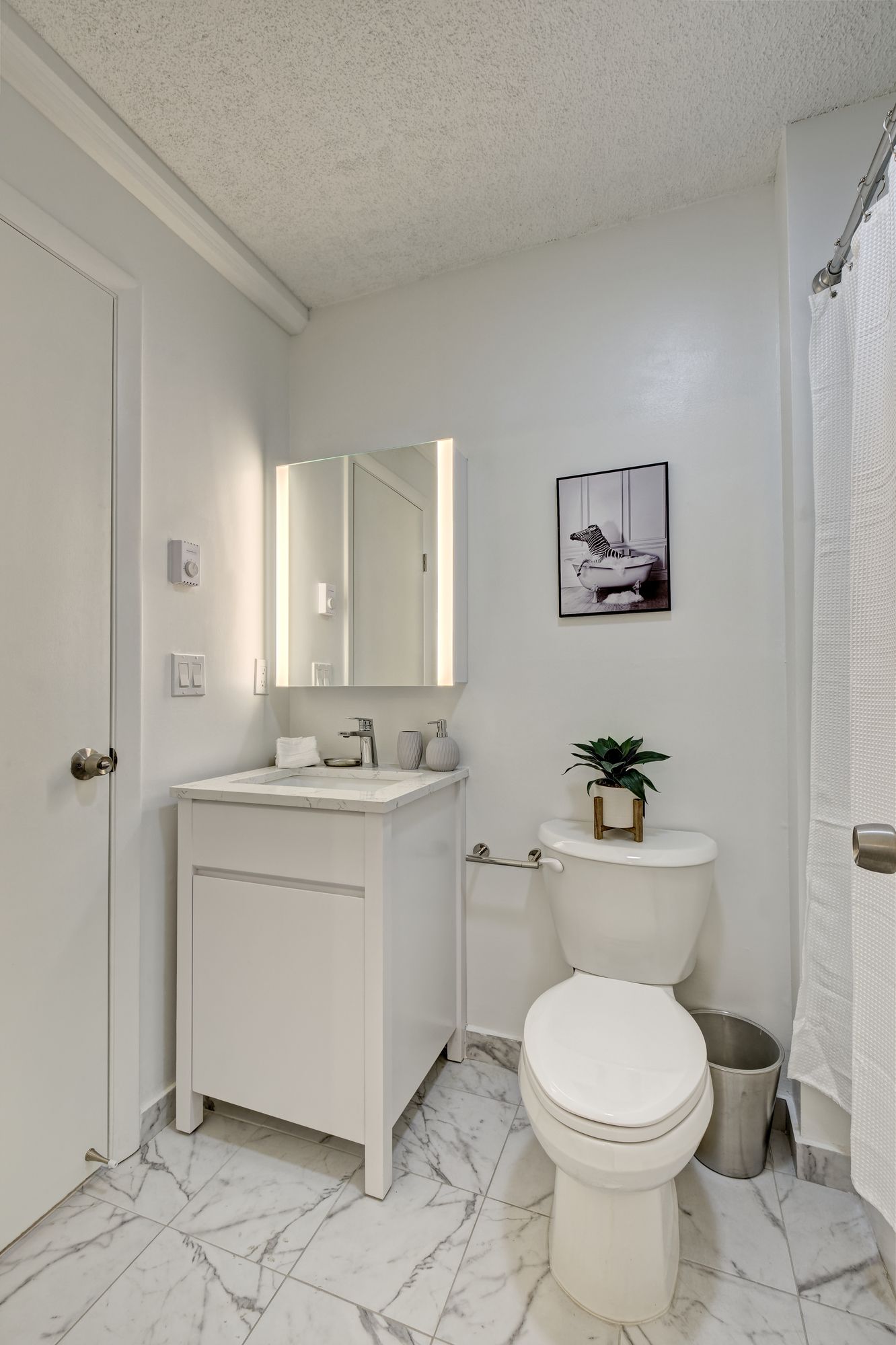 White bathroom with a vanity, toilet, and marble floor.