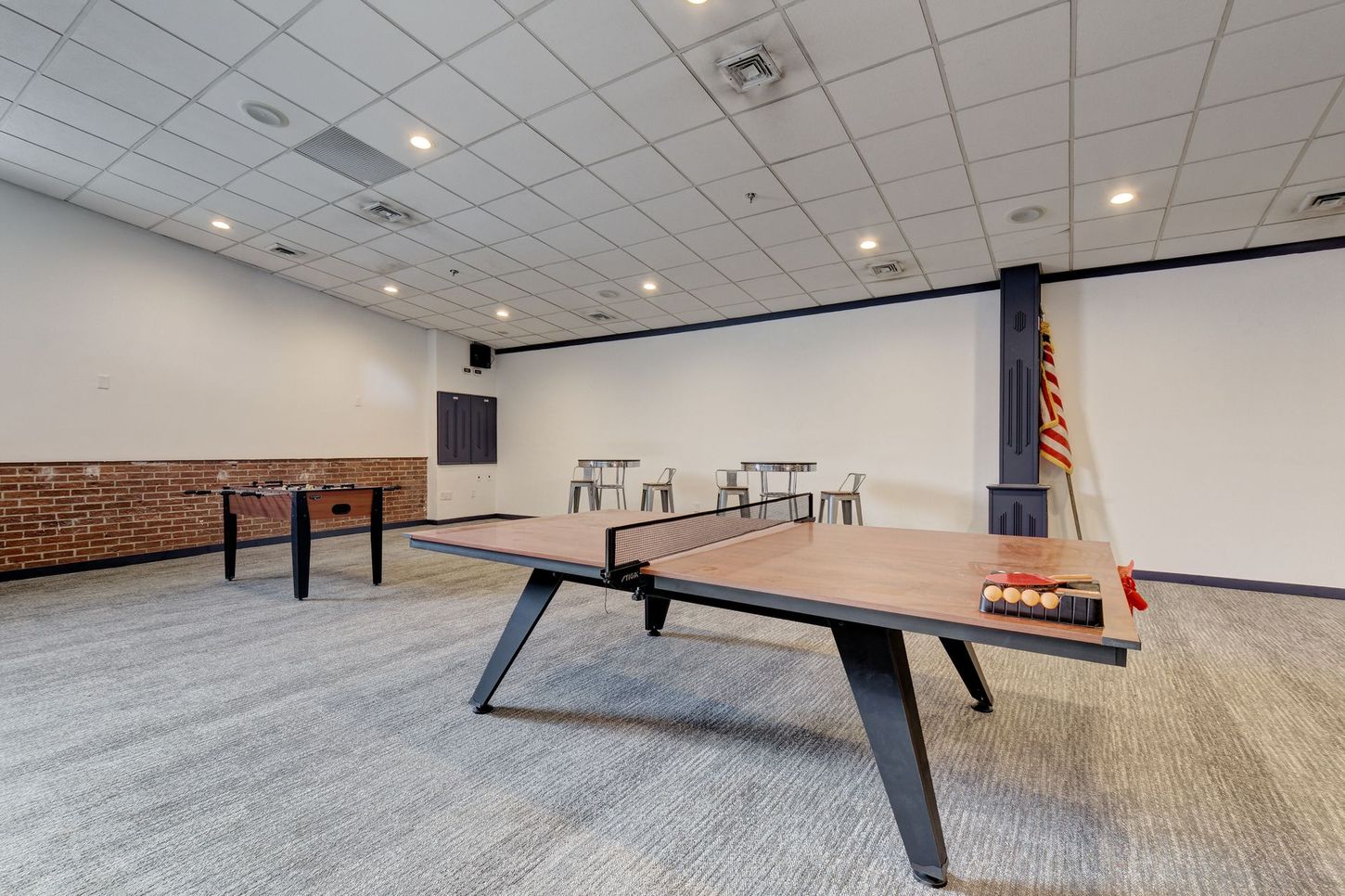 A game room featuring a ping pong table, foosball, high-top seating, and a decorative wall.