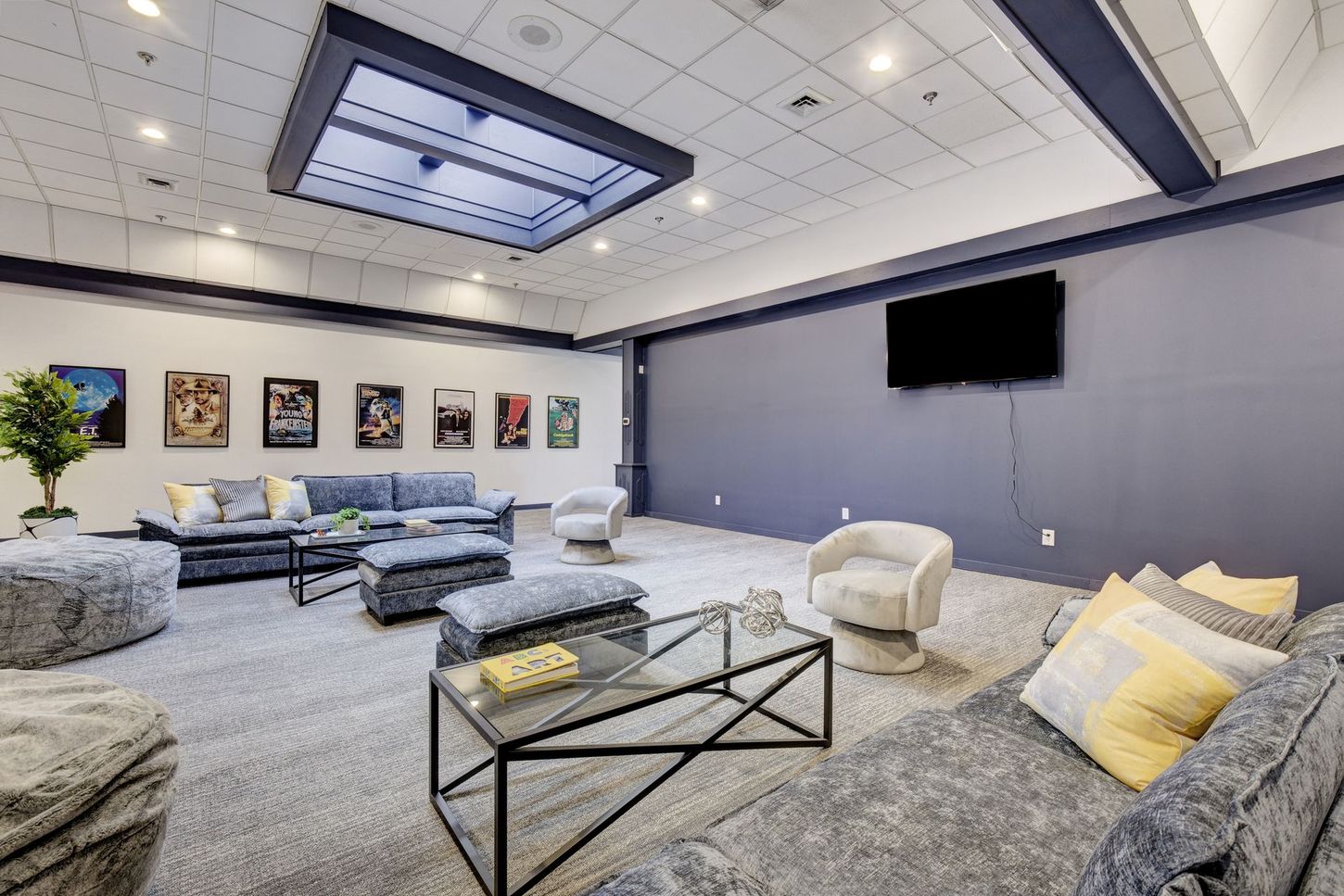 A modern lounge with grey sofas, a large TV, movie posters, and a skylight.