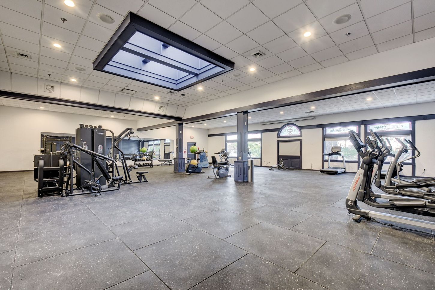Gym interior with exercise machines, dark floor, and bright overhead lights.