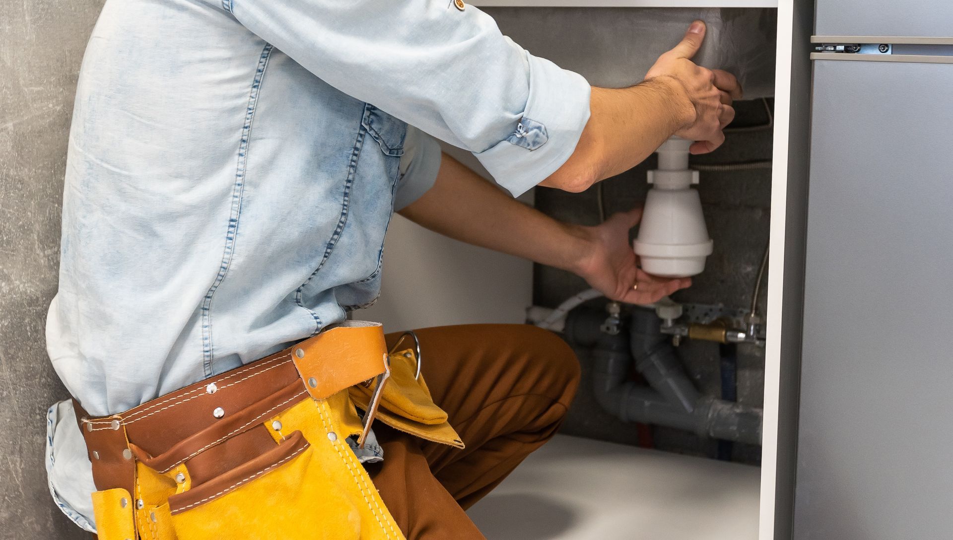 A plumber is fixing a sink in a kitchen.