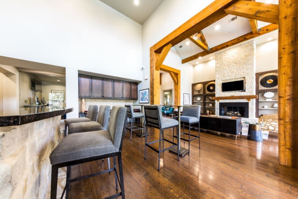 Clubhouse with a kitchen bar, chairs, tables, and a fireplace at Marquis at Sugar Land in Sugar Land, TX.