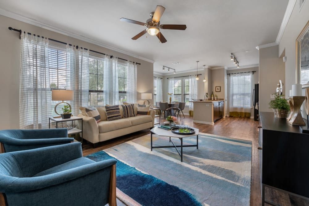 A spacious living room filled with furniture and a ceiling fan surrounded by windows with natural light at Marquis at Sugar Land in Sugar Land, TX.