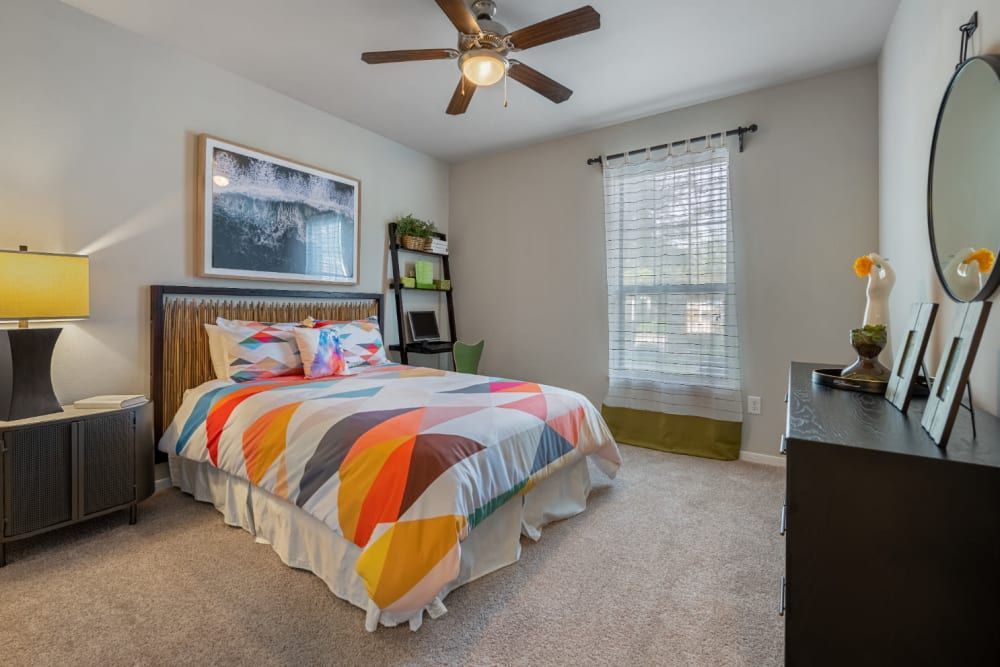 Apartment bedroom with a bed, dresser, wall art, window, and ceiling fan at Marquis at Sugar Land in Sugar Land, TX.