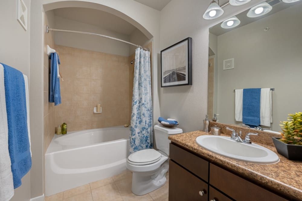 Apartment bathroom with a tub, toilet, sink and mirror at Marquis at Sugar Land in Sugar Land, TX.