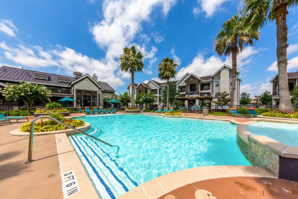 Resort-style swimming pool in front of apartment buildings with palm trees at Marquis at Sugar Land in Sugar Land, TX.