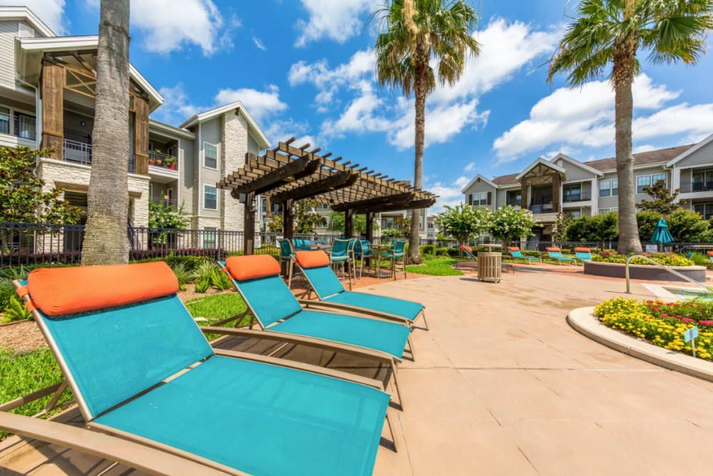 A row of lounge chairs are lined up in front of a swimming pool  at Marquis at Sugar Land in Sugar Land, TX.