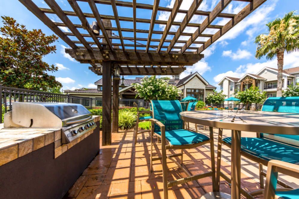 A patio with an outdoor table and chairs and a grill under a pergola at Marquis at Sugar Land in Sugar Land, TX.