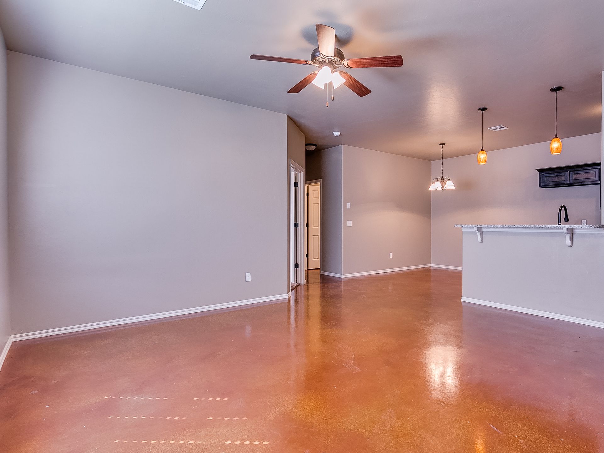Open-concept living space with brown floors, neutral walls, ceiling fan, and a kitchen bar.