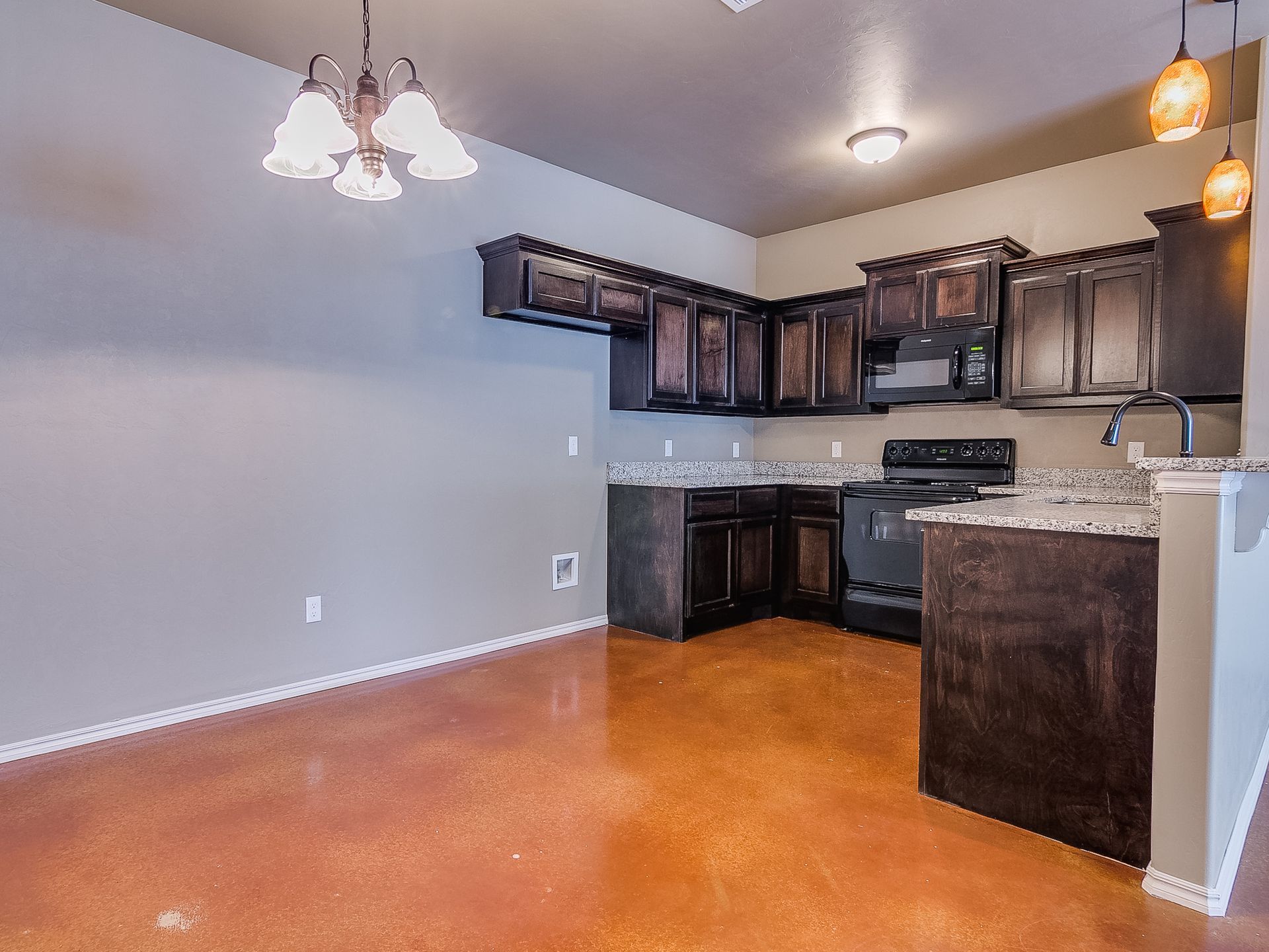 Kitchen with brown cabinets, stove, speckled countertop, and shiny orange floor.