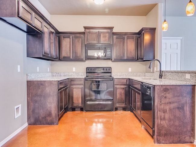 Kitchen with dark cabinets, granite countertops, black appliances, and orange-toned flooring.
