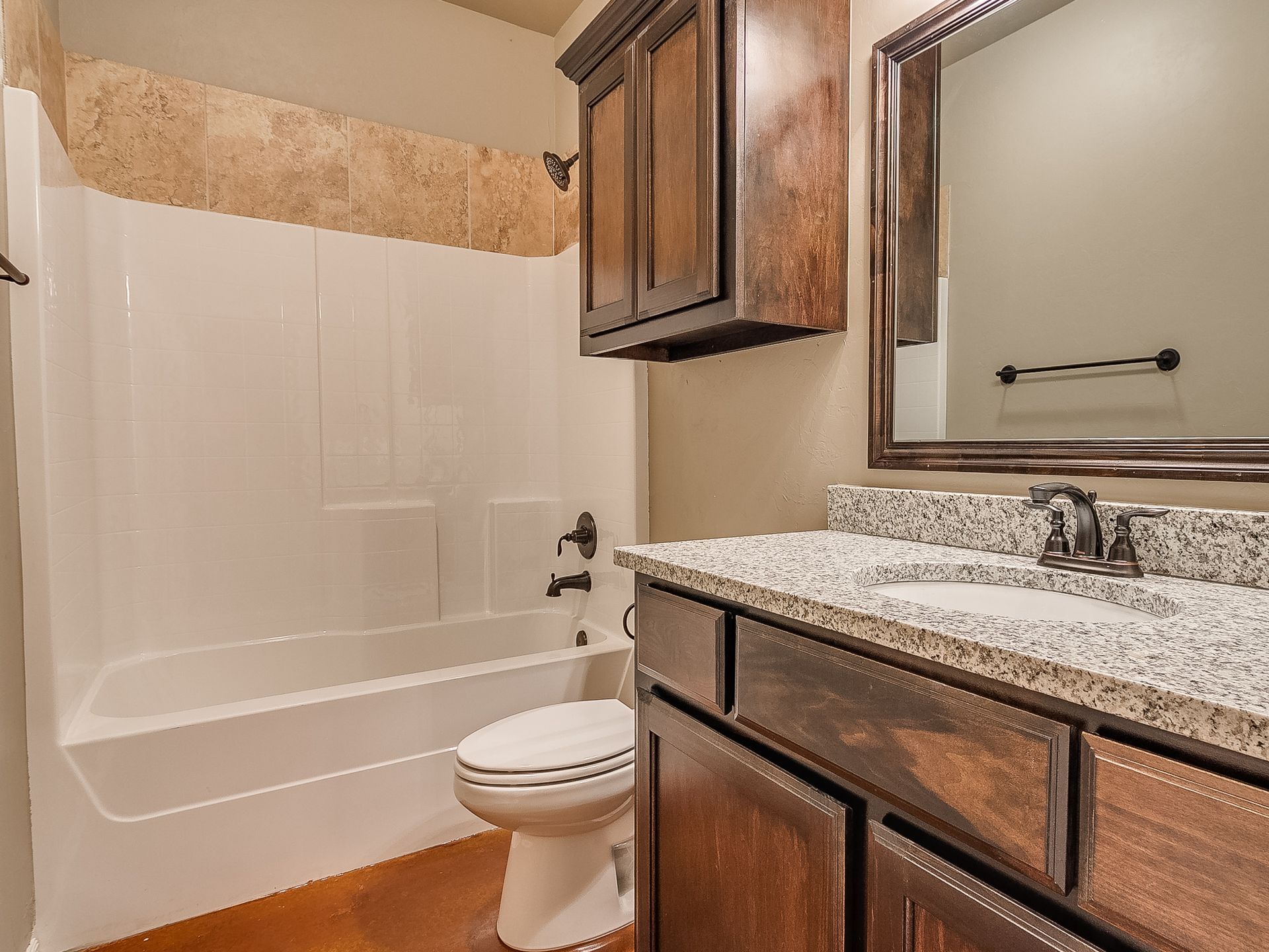 Bathroom with a tub, toilet, vanity, and dark wooden cabinets. Light-colored walls and floor.