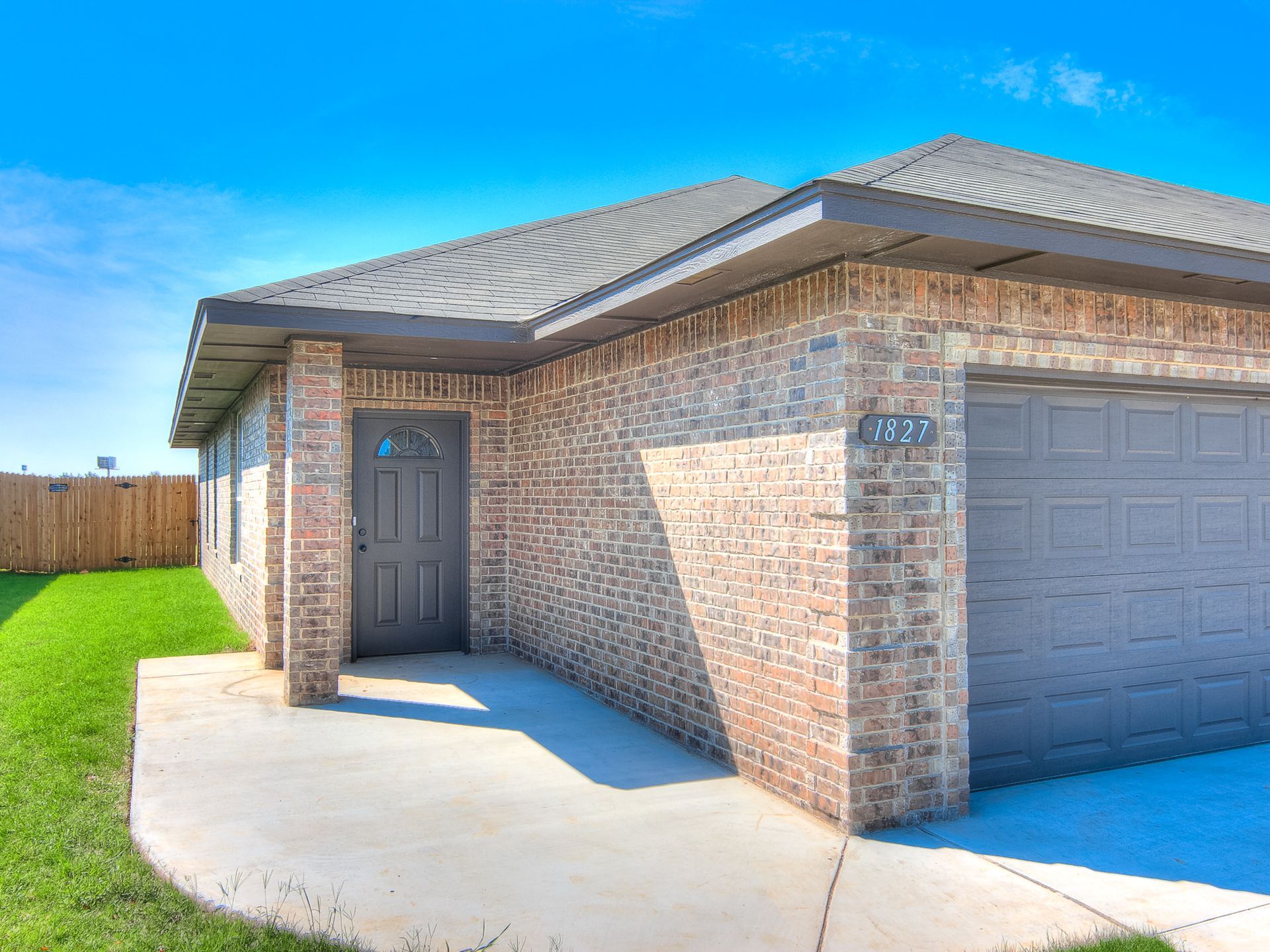 Brick house with a gray door, garage, and green lawn under a blue sky.