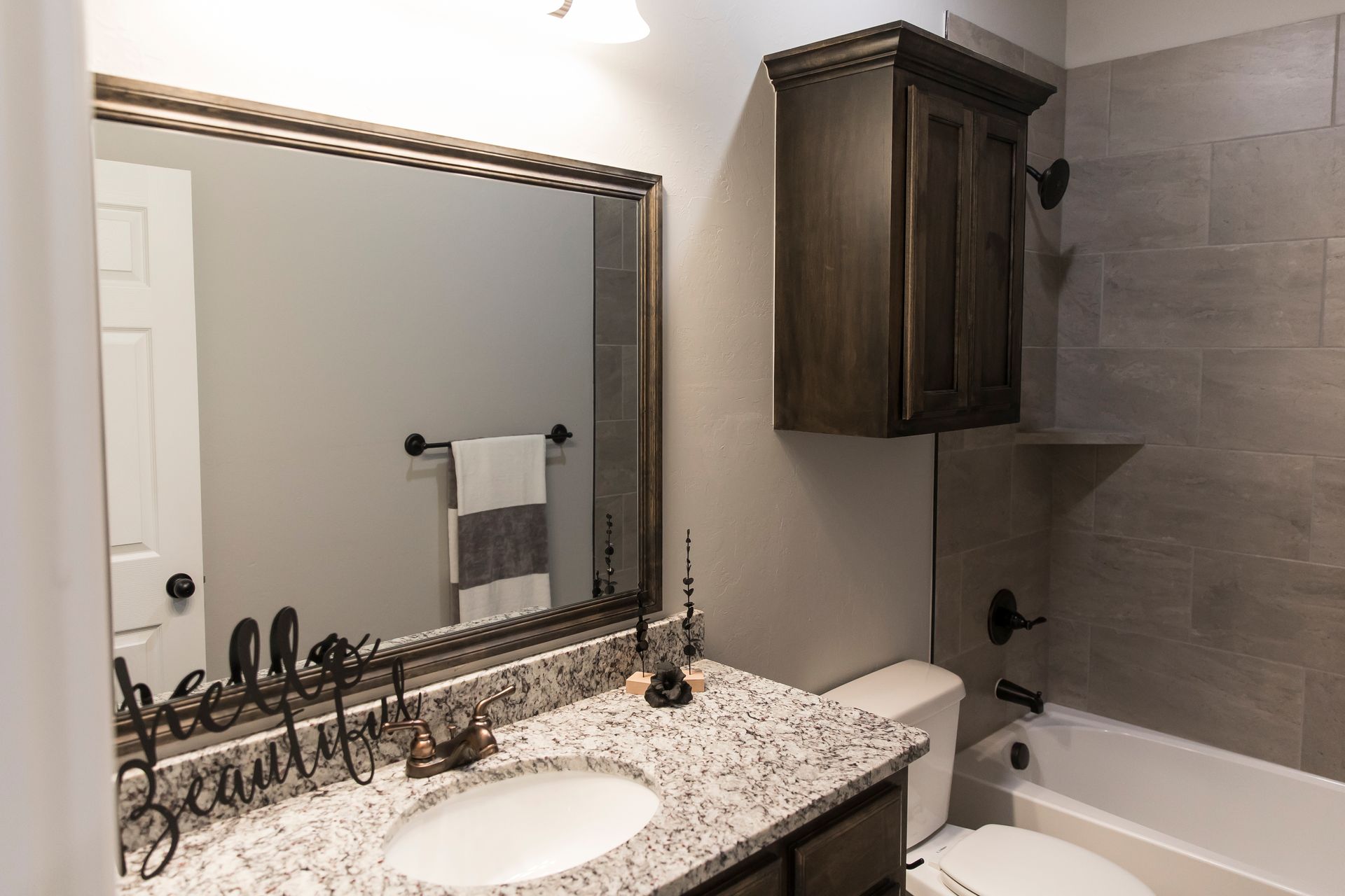 Bathroom with gray walls, granite countertop, dark brown cabinets, and large mirror.