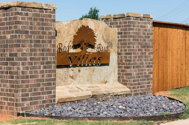 Entry sign for Red Bud Villas, brick pillars framing a stone slab with a metal tree and text.