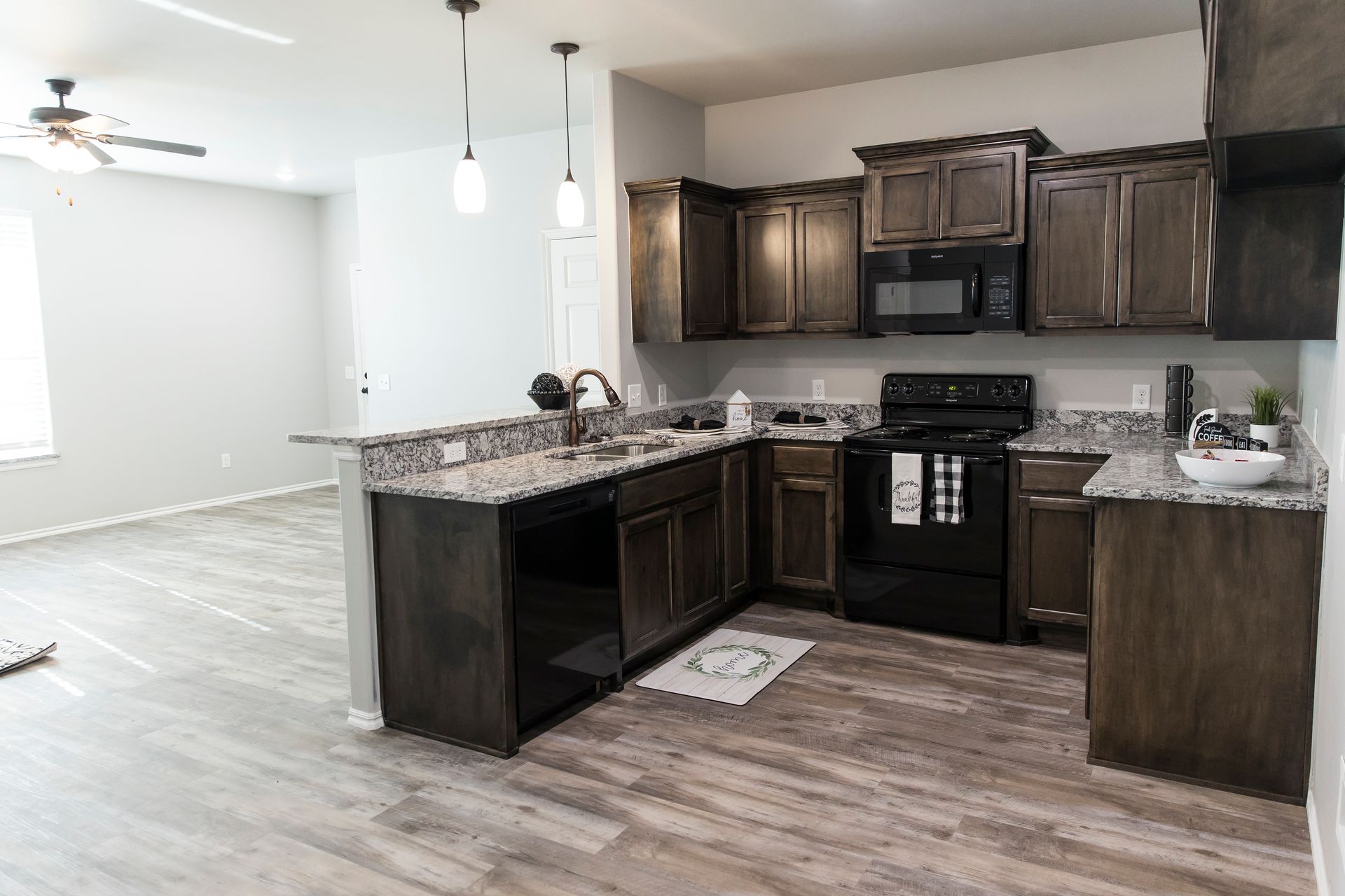 Kitchen with dark cabinets, granite countertops, black appliances, and light wood-look floors.
