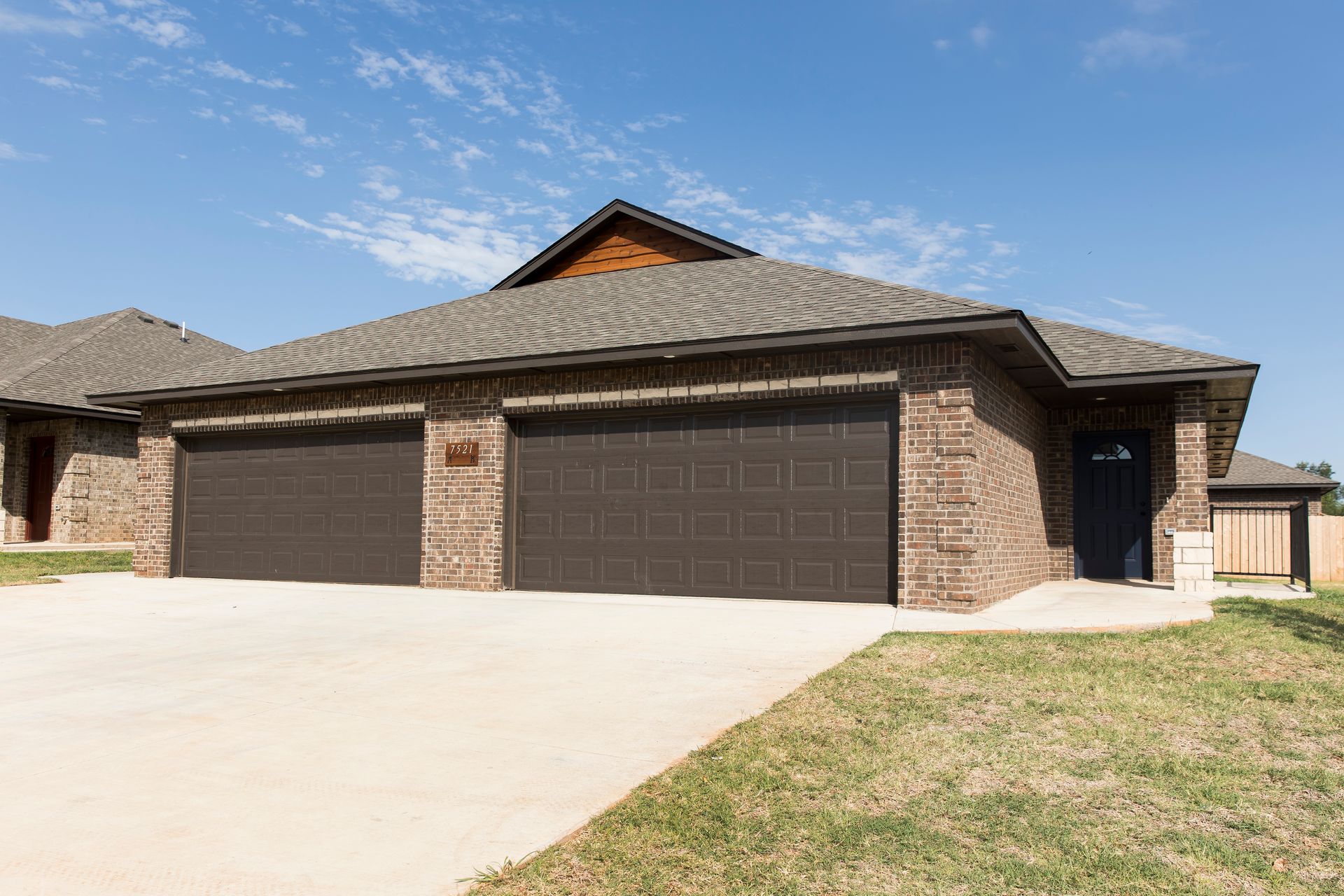 Brick house with two-car garage and brown doors under a blue sky.