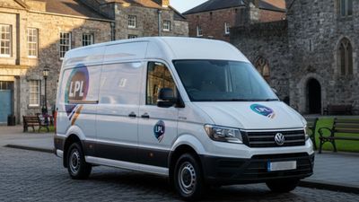 White Volkswagen van with LPL logo parked on a cobblestone street in front of a stone building.