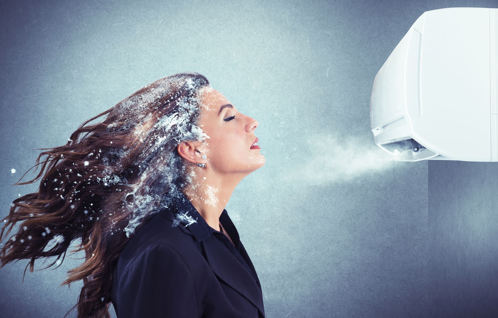 A woman is standing in front of an air conditioner with her hair blowing in the wind.