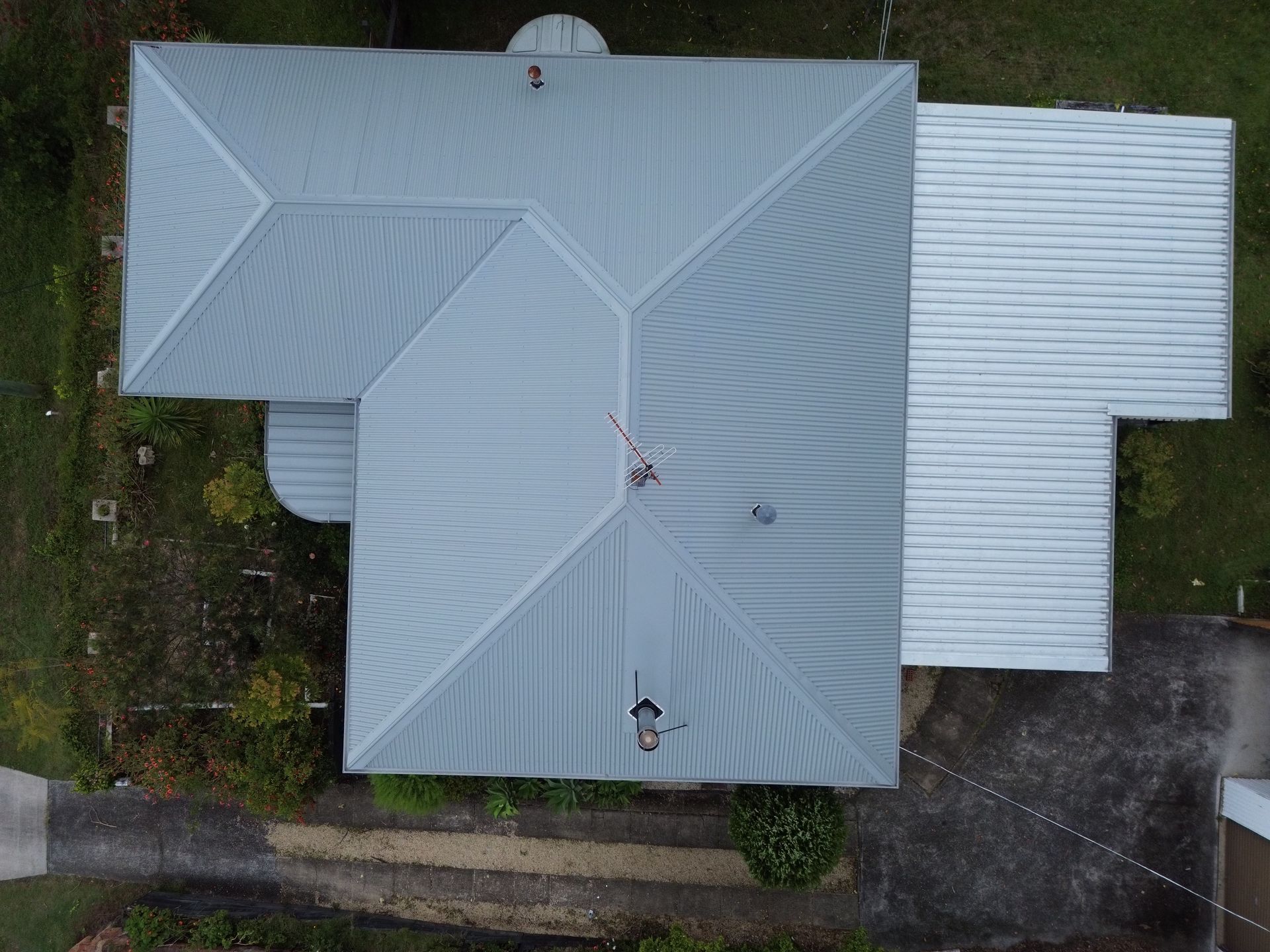 Overhead view of a house with a gray roof and asphalt driveway, surrounded by greenery. - Ace1 Metal Roofing