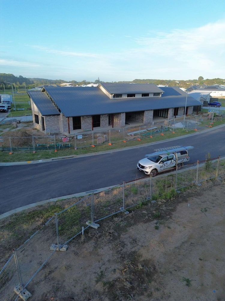 Long, Low House Under Construction, Grey Roof, White Vehicle Driving on a Road — ACE1 Metal Roofing in Taree, NSW