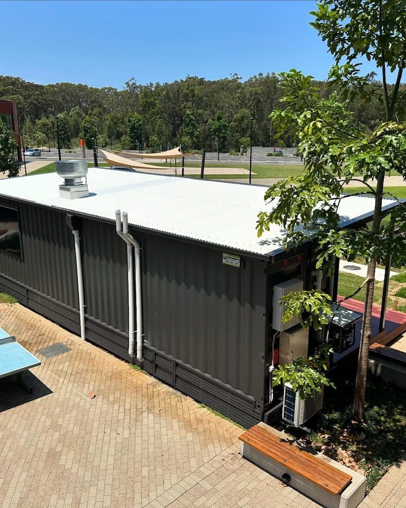 A Dark Grey Rectangular Building With a White Roof in an Outdoor Setting — Ace1 Metal Roofing in Taree, NSW