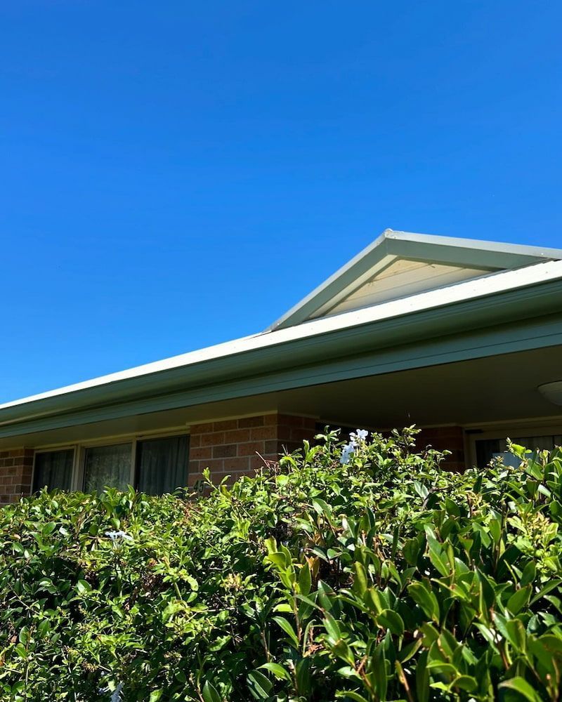 Blue Sky Over a Brick Building With Green Bushes and White Trim — Ace1 Metal Roofing in Taree, NSW