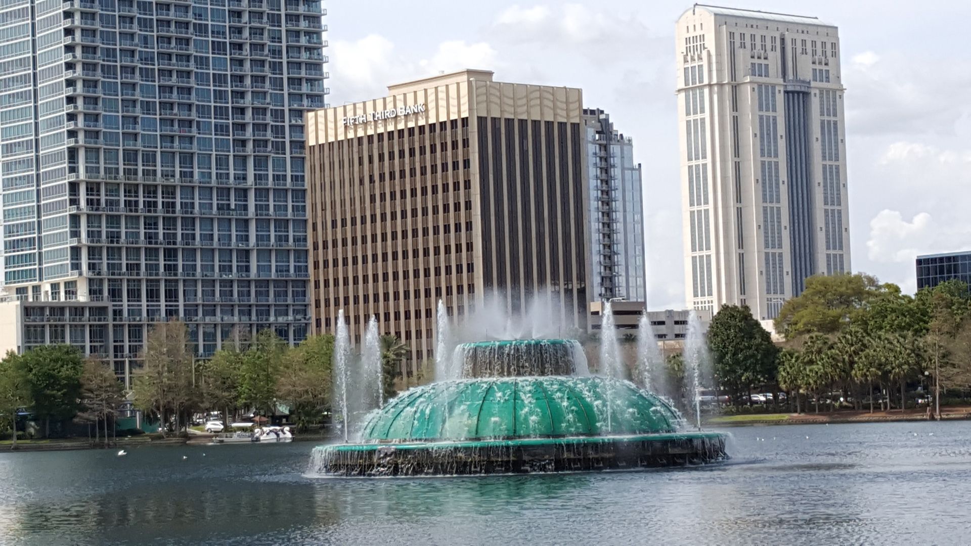 Fountain in a lake with downtown Orlando buildings in the background on a sunny day.