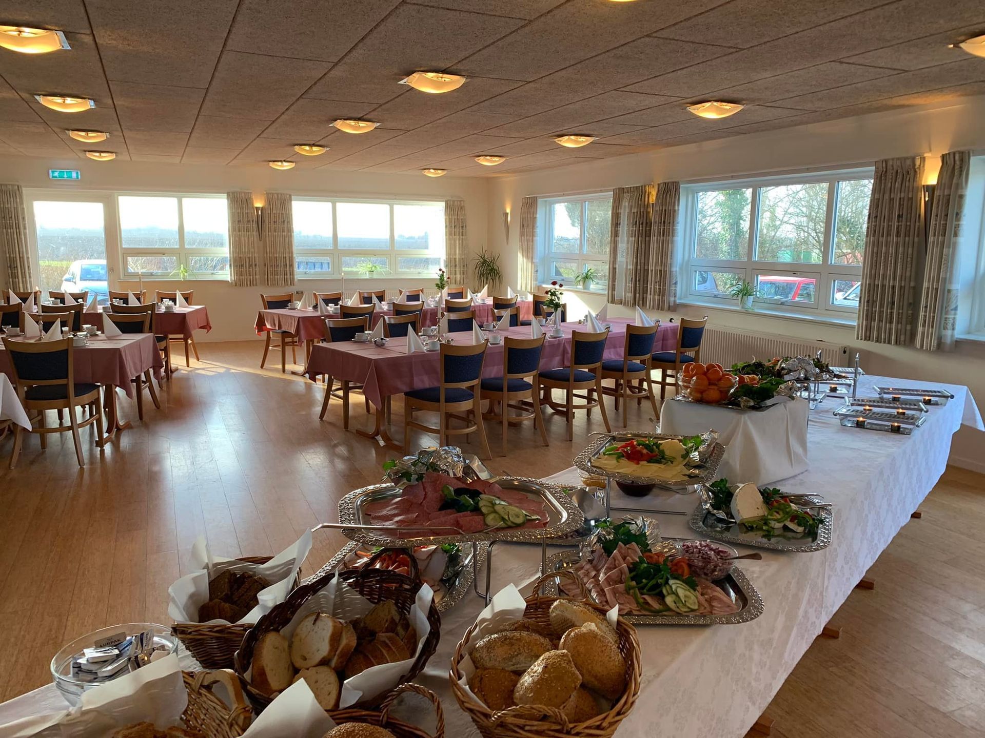 Buffetbord med mad og spiseborde med stole i en godt oplyst restaurant.