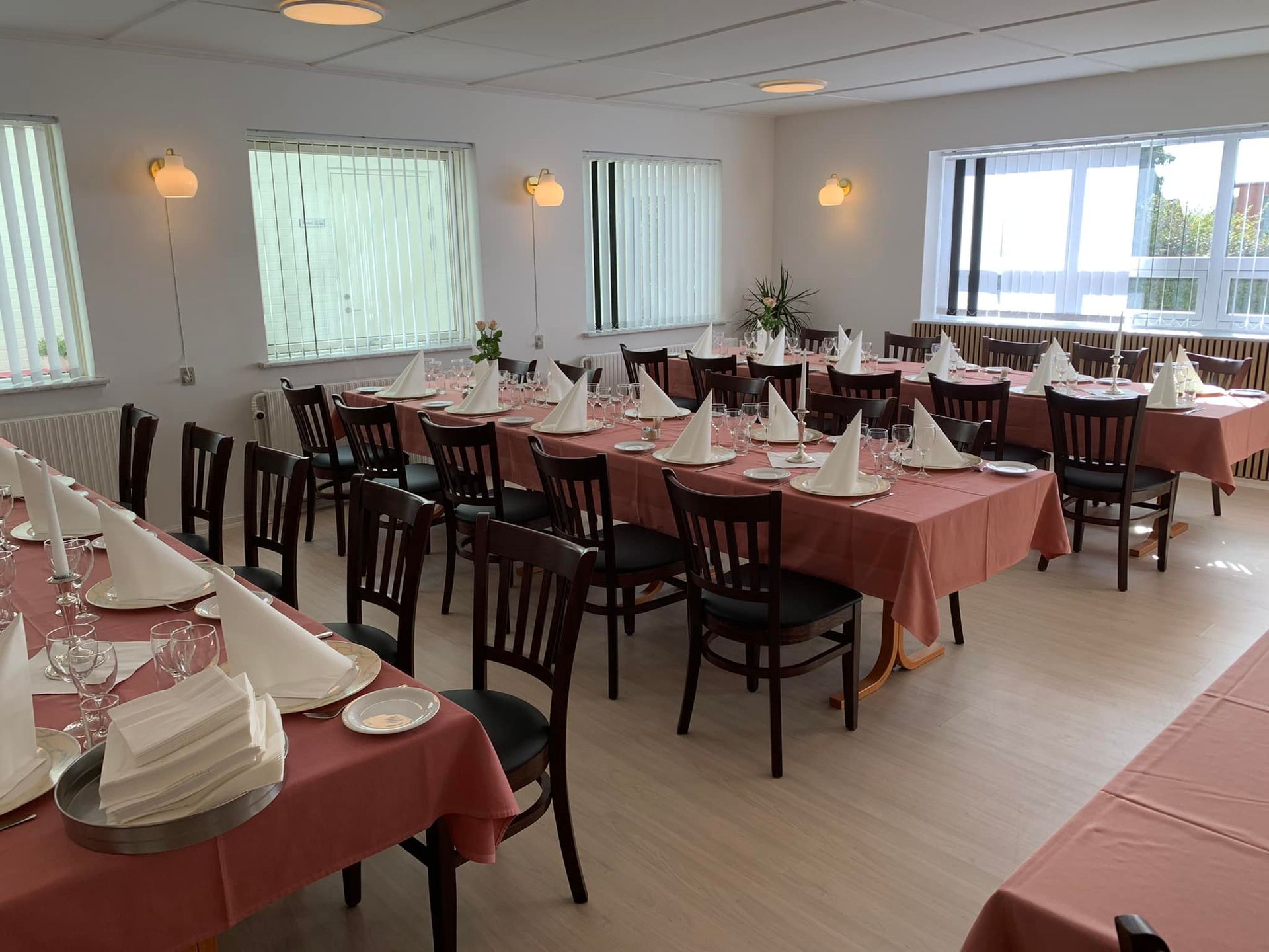 selskabslokale med dækkede borde til et måltid med lyserøde duge, hvide servietter og mørke træstole.