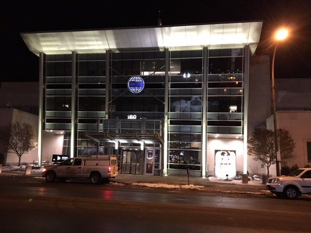 Front of a modern building at night, illuminated, with a sign and a service truck parked nearby.