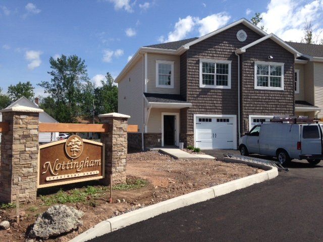 Nottingham apartment complex entrance sign and townhouses; tan siding, brown shake siding, and blue sky.