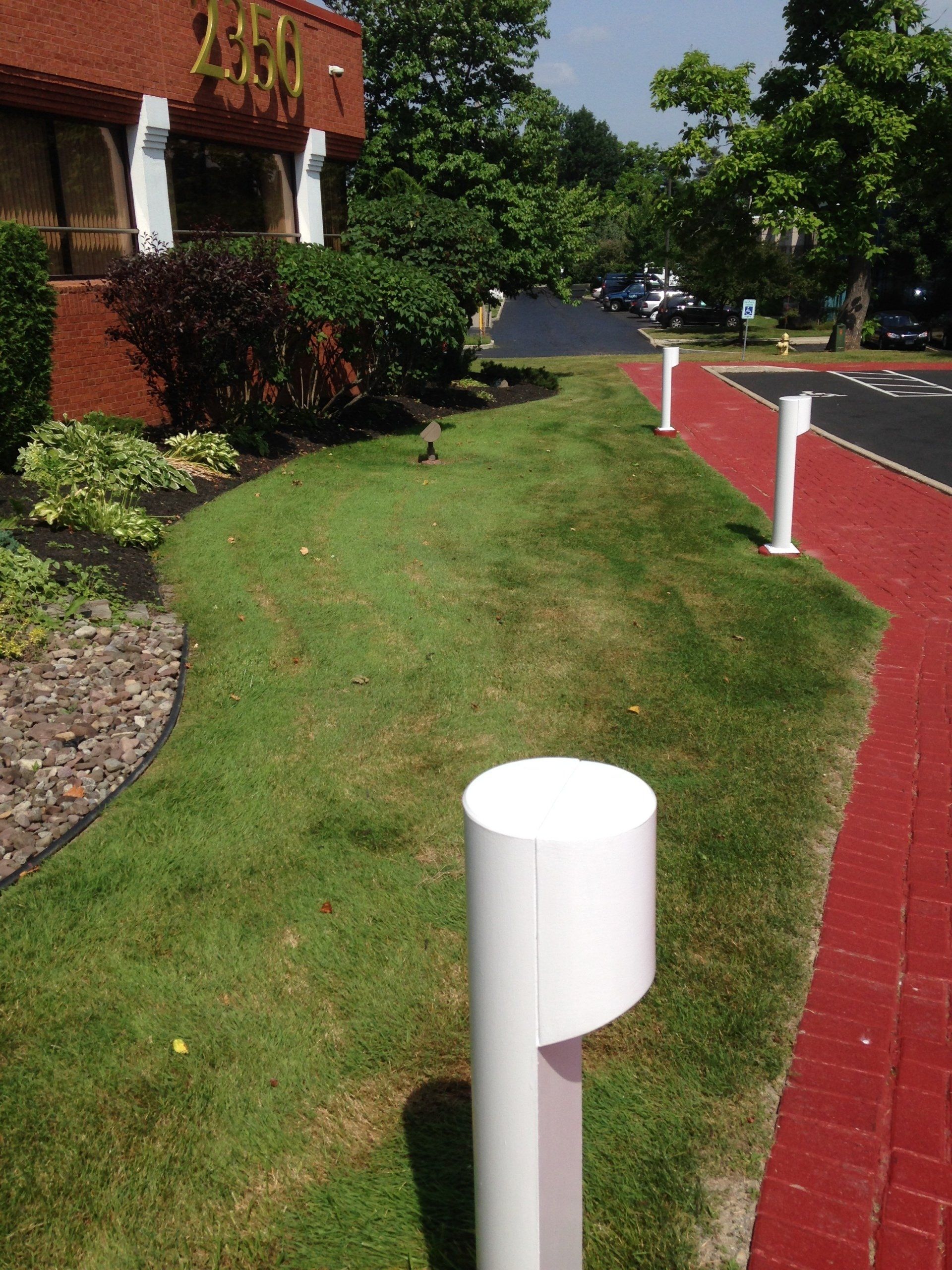 Exterior view of a building with a lawn, red walkway, and white cylindrical lights.