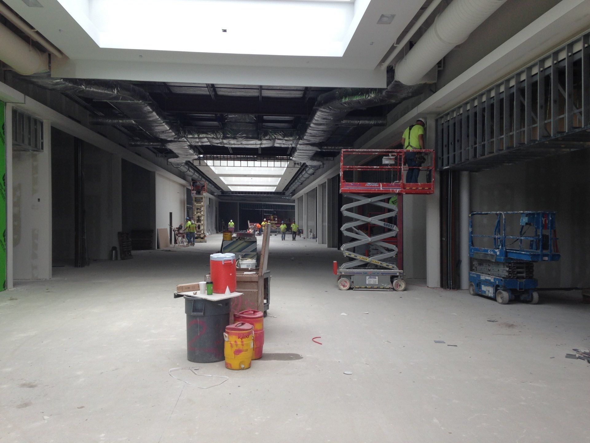 Construction site: workers on lifts, unfinished corridor, exposed ducts and framework, concrete floor, skylight.