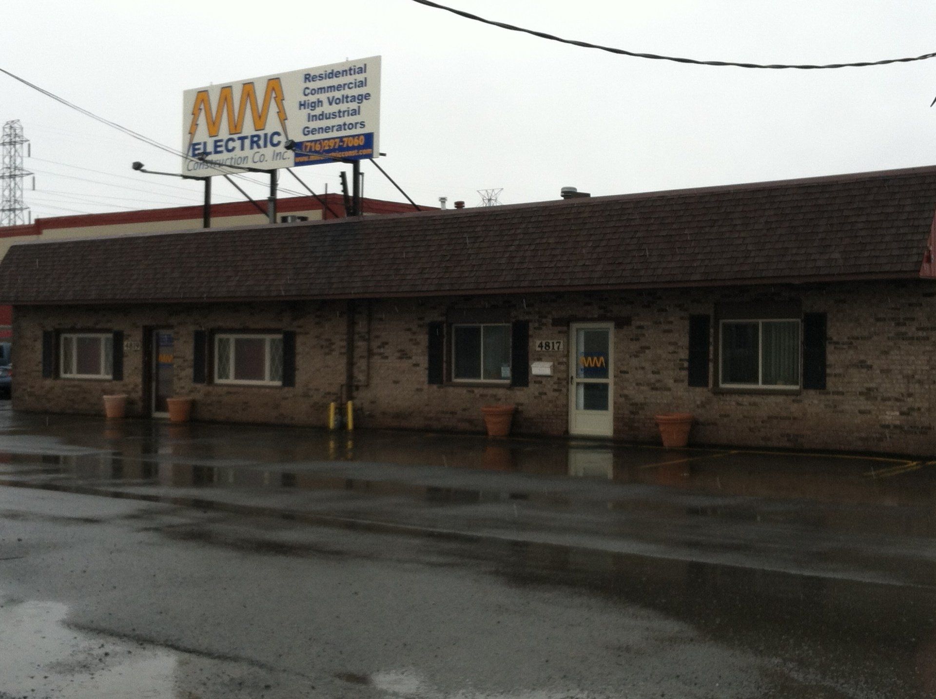 Brick building with black windows and a brown roof; MM Electric sign overhead.