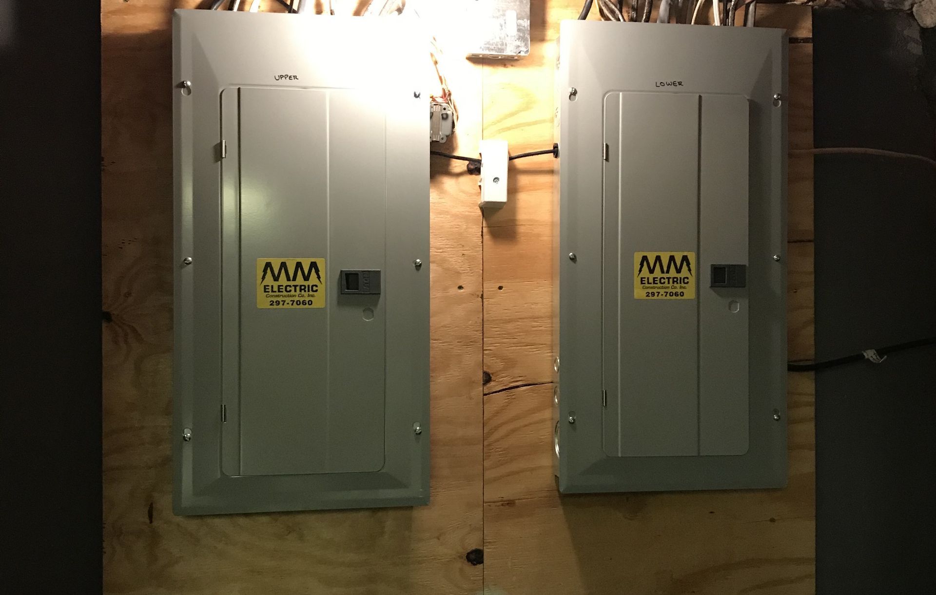 Two gray electrical panels mounted on wood paneling, each with a warning label and a handle.