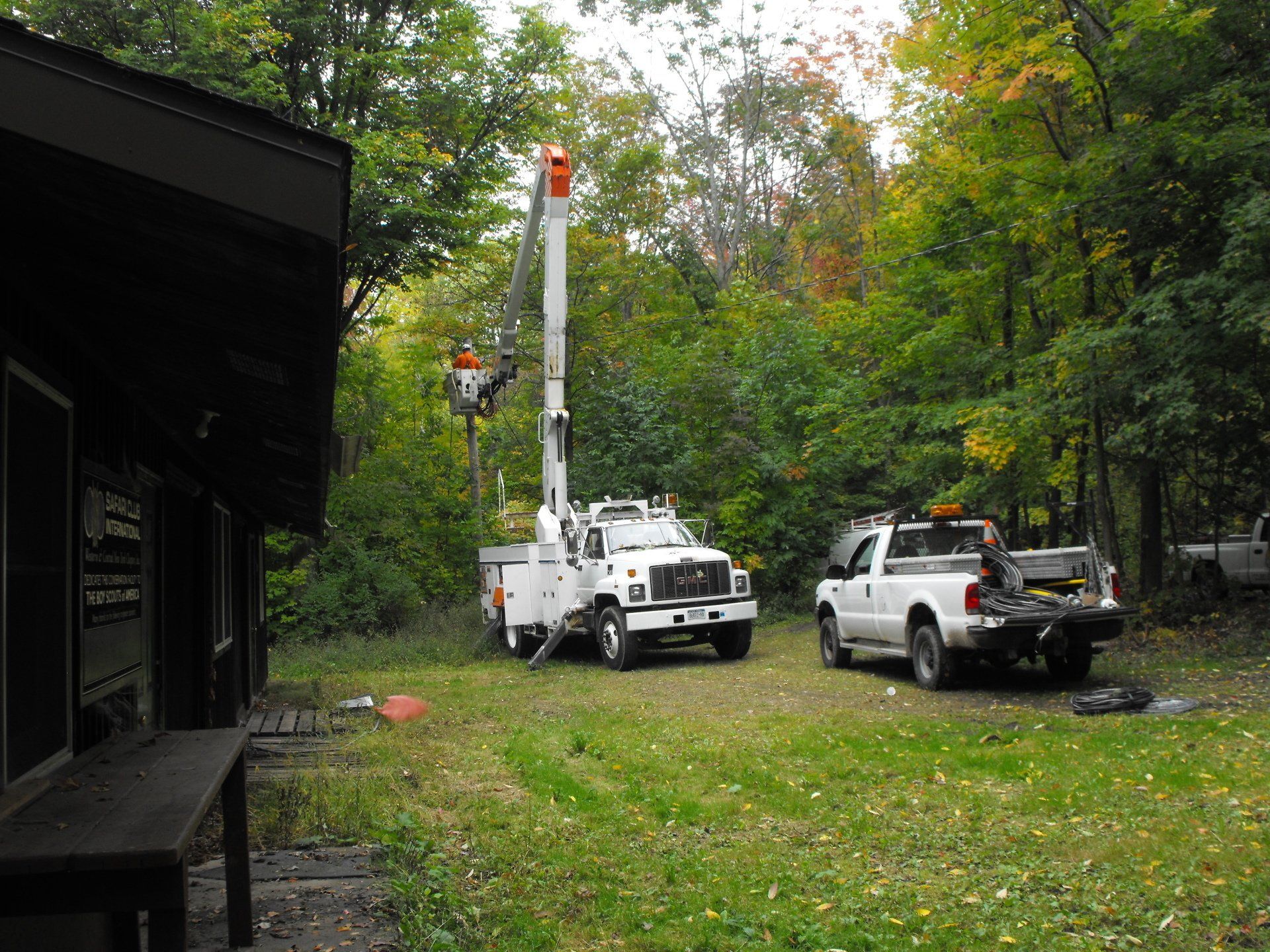 A tree-trimming truck and crew in a grassy area next to a building and trees.