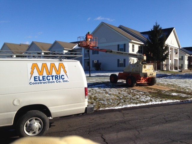 White van from MM Electric, worker in lift working on the side of a multi-unit building.
