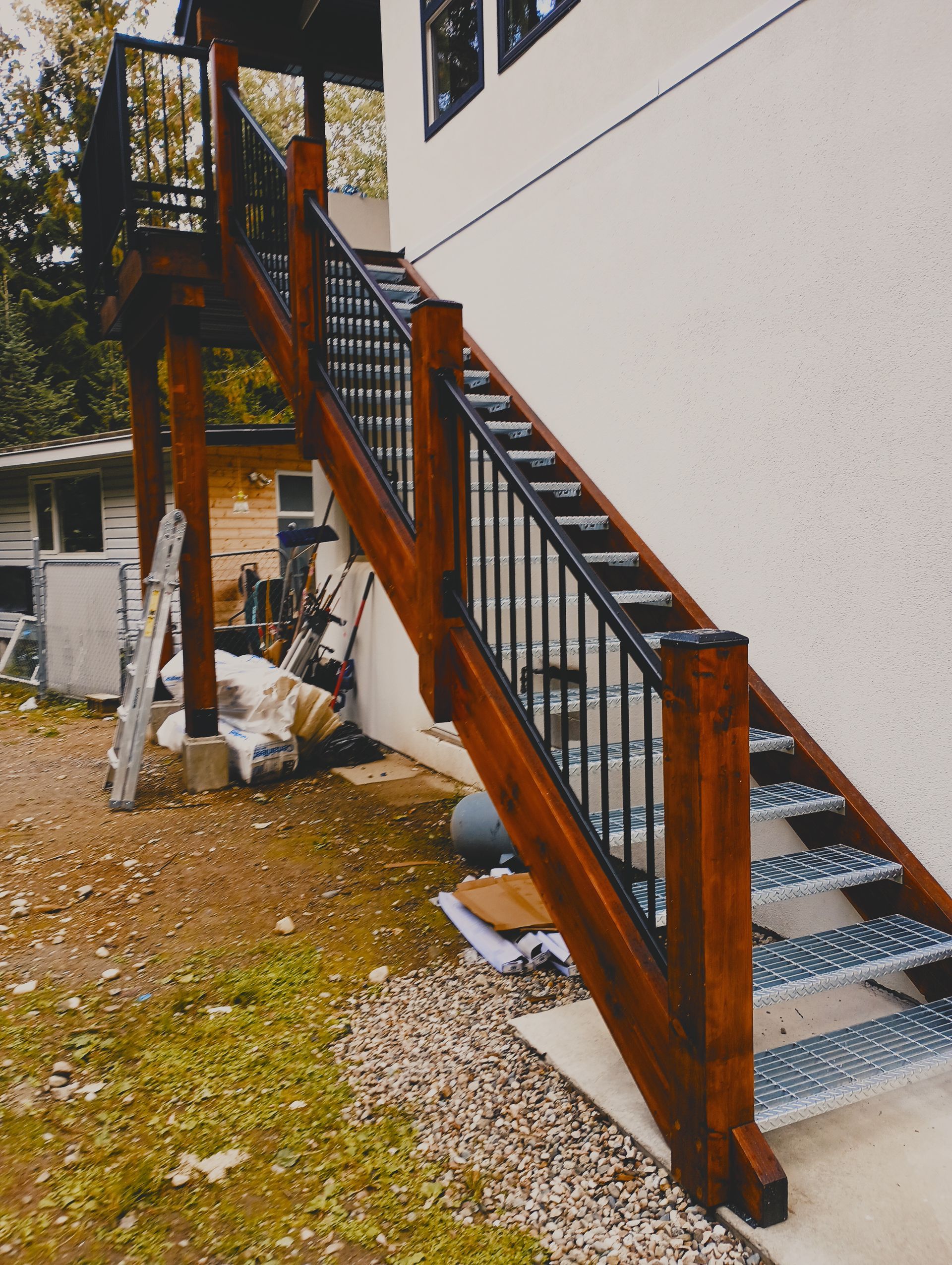 Outdoor wooden staircase with black metal railings leading up to a house exterior.